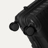 Close-up detail view of the Optima Expandable Medium Check-in Spinner in Black, showcasing the self-aligning spinner wheels and the reinforced corner construction.